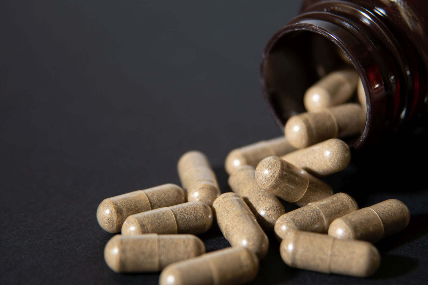 Herbal capsules poured from a jar on a dark production surface